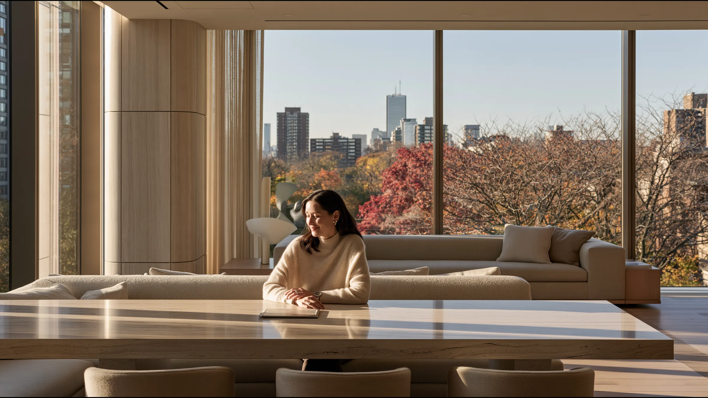 A clinic owner alone at a long travertine table in a double-height private clinic lounge in Yorkville, Toronto, a single tablet before her, a slow smile of satisfaction