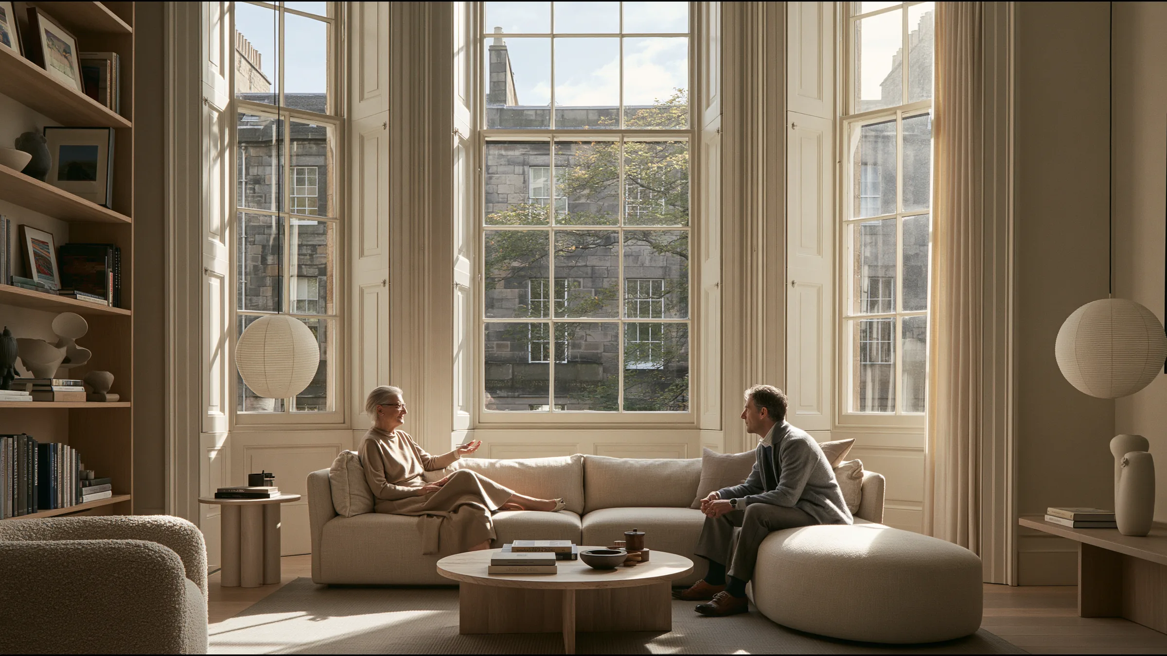A doctor seated with a patient in her seventies on a deep linen sofa in a grand Georgian consulting room in Edinburgh New Town, tall sash windows of soft northern light, the patient nodding with reassurance, art and books on oak shelves
