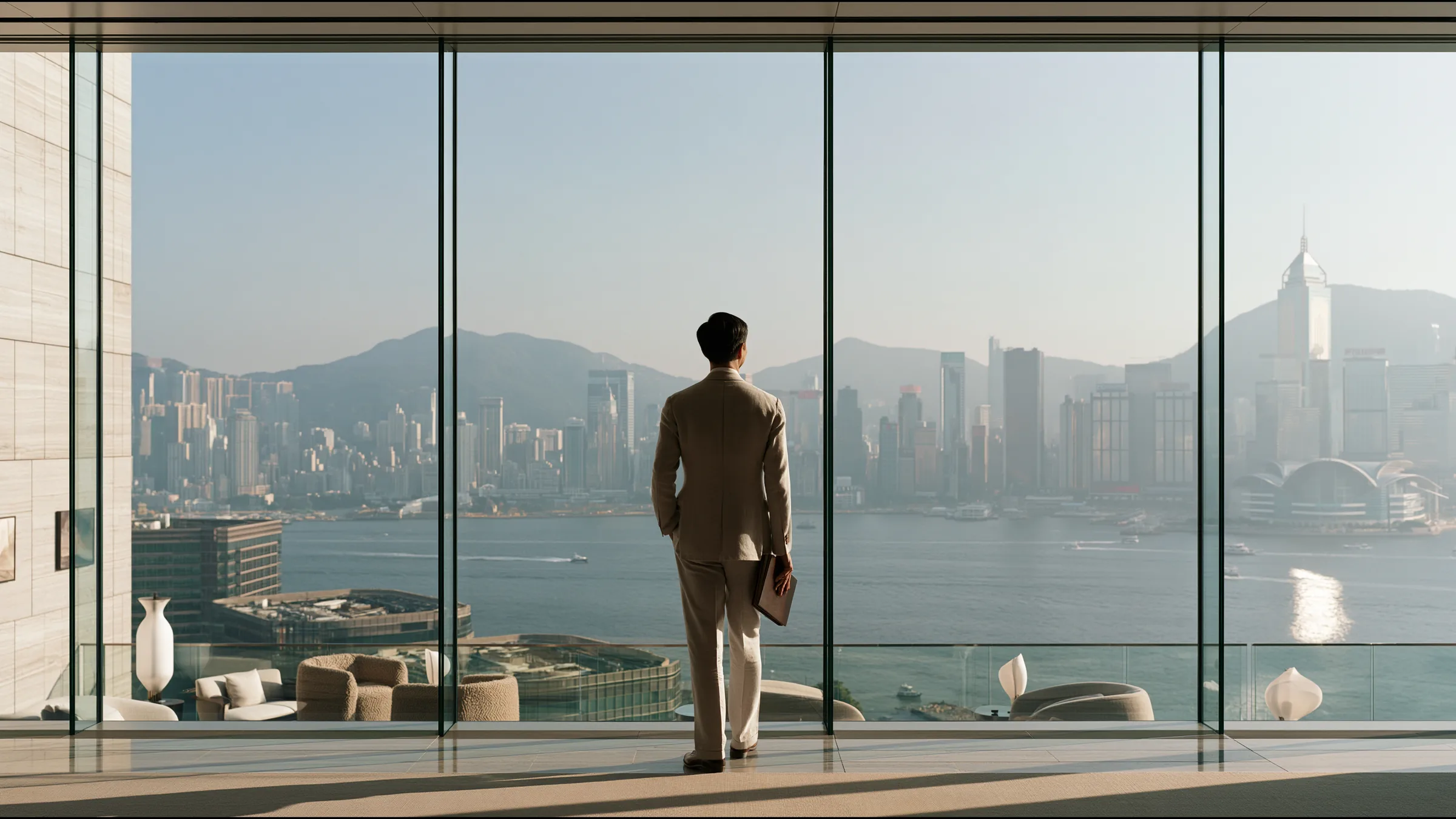 A medical director standing alone at a wall of glass in a calm double-height clinic in Central, Hong Kong, holding a single bound document, the harbour and the Peak in clear light