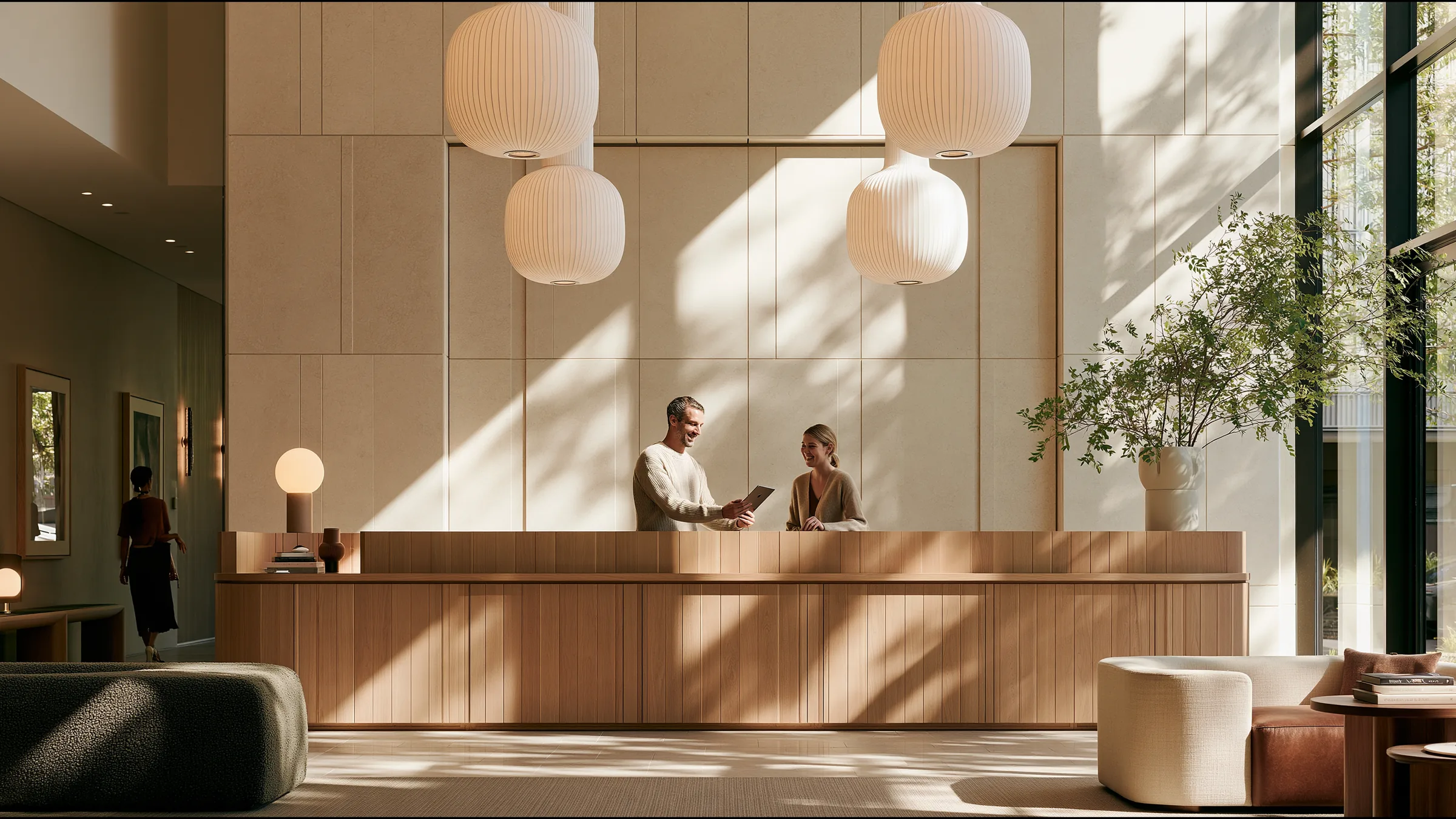 A clinician in fine knit showing a colleague a tablet at a long timber reception counter in a vast light-filled Surry Hills clinic in Sydney, both smiling, sculptural pendant lights and greenery