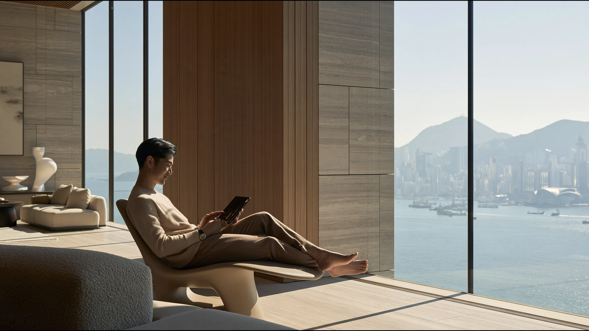 A clinic lead in fine knit on a video call on a tablet, seated on a sculptural chair in a calm double-height office in Central, Hong Kong, smiling with relief