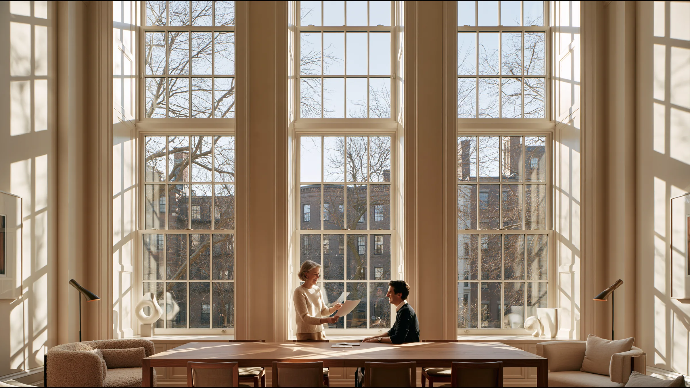 A clinic medical director in her fifties in fine knit standing at a long oak table in a grand Back Bay townhouse clinic in Boston, presenting a single page to one partner, both smiling, tall windows