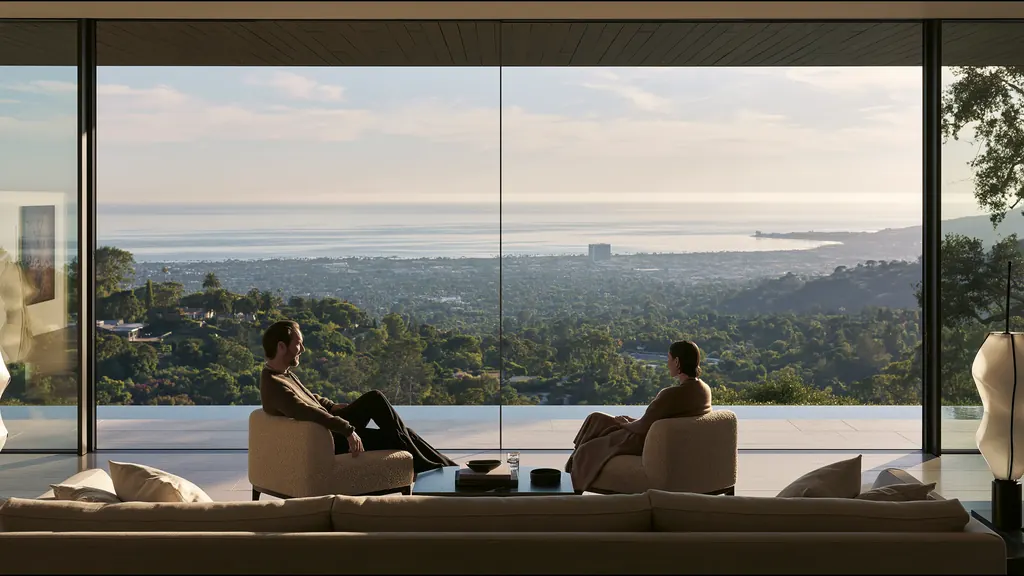Two people talk in armchairs in a glass-walled room above wooded California hills, the Pacific on the horizon